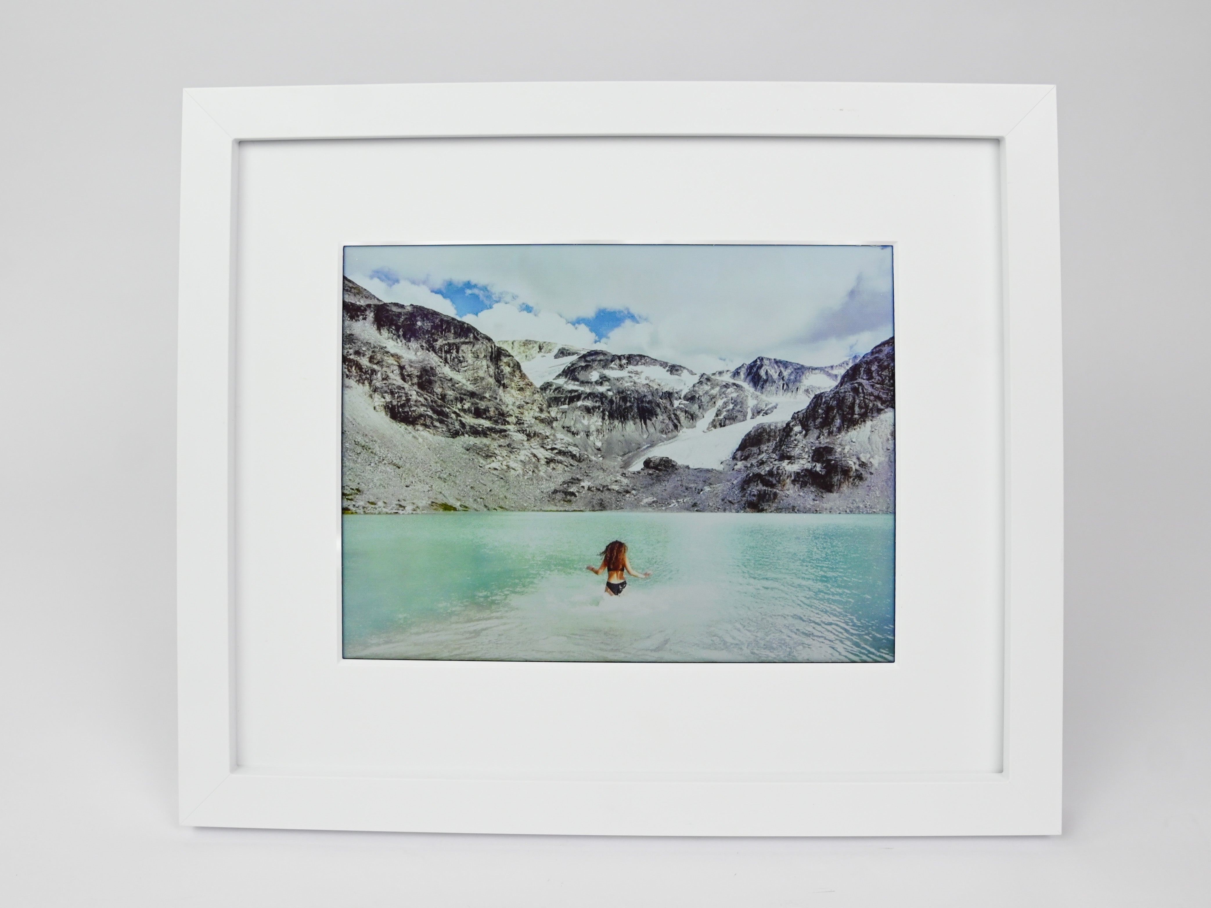 Framed photograph of a person in a hot spring with mountains in the background #white