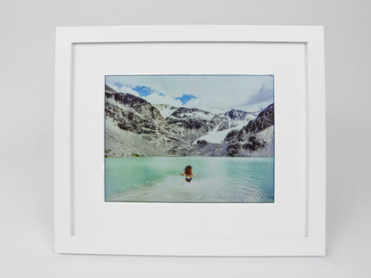 Framed photograph of a person in a hot spring with mountains in the background #white